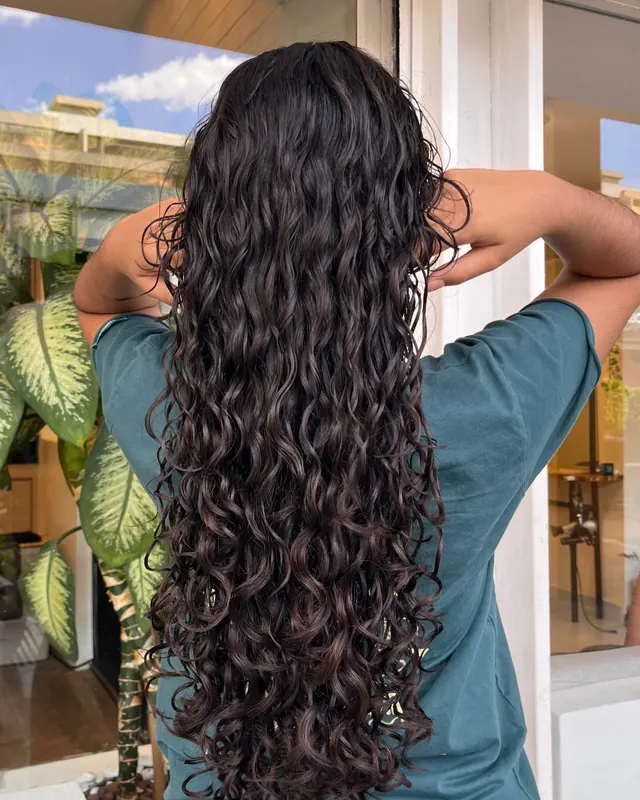 Cabelo longo com cachos definidos, castanho-escuro, visto de costas diante da vitrine do salão
