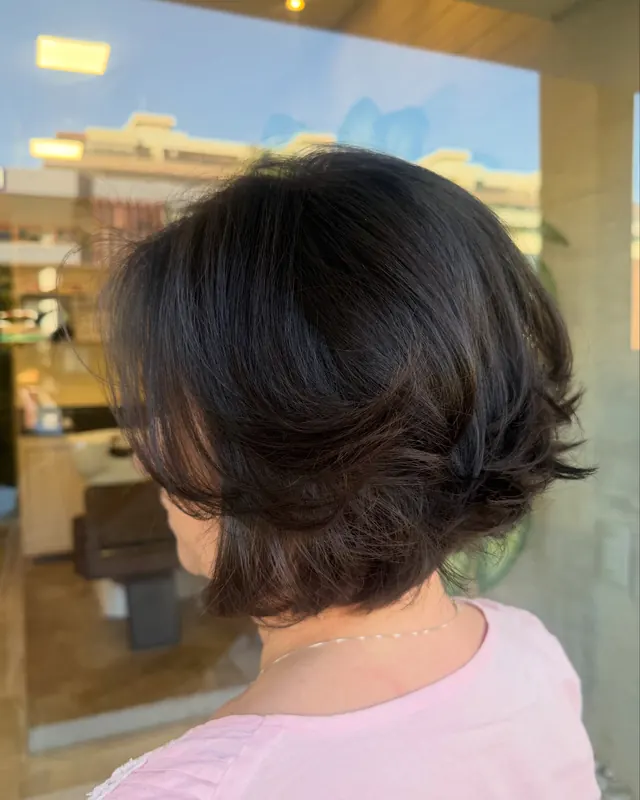 Corte curto em camadas, castanho-escuro, visto de costas, com a vitrine do salão ao fundo