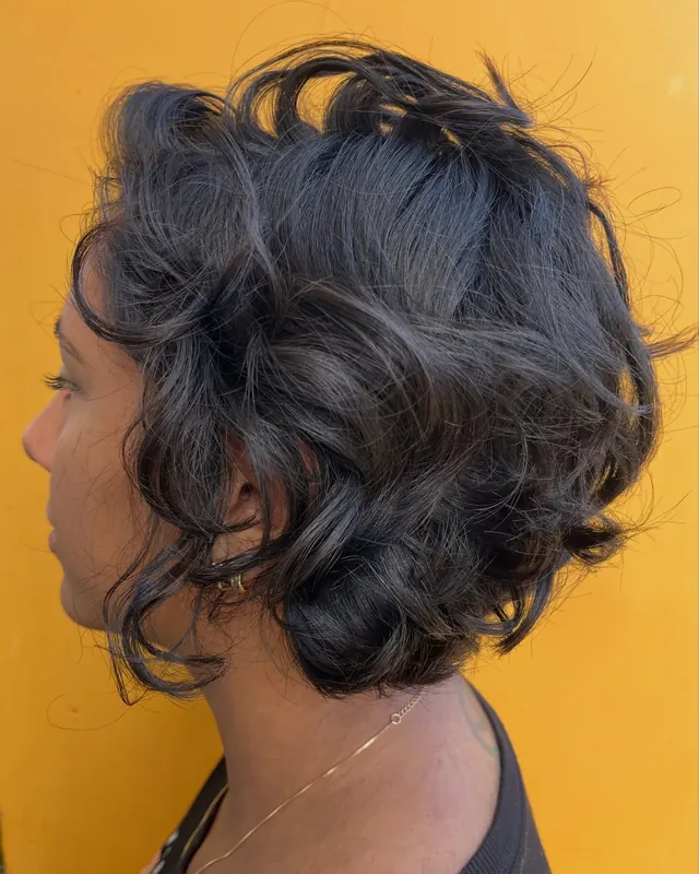 Cabelo curto ondulado e escuro, de perfil, diante de uma parede amarela