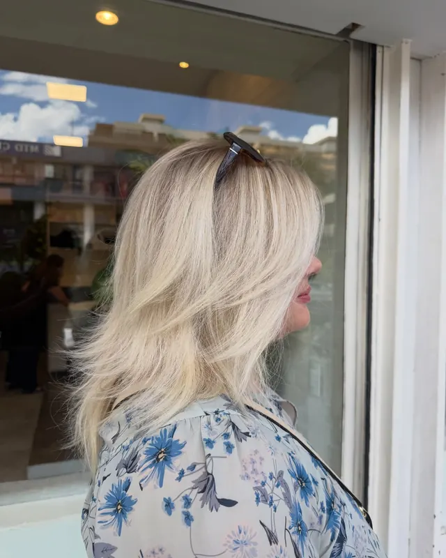 Cabelo loiro perolado em camadas, de perfil, diante da vitrine do salão